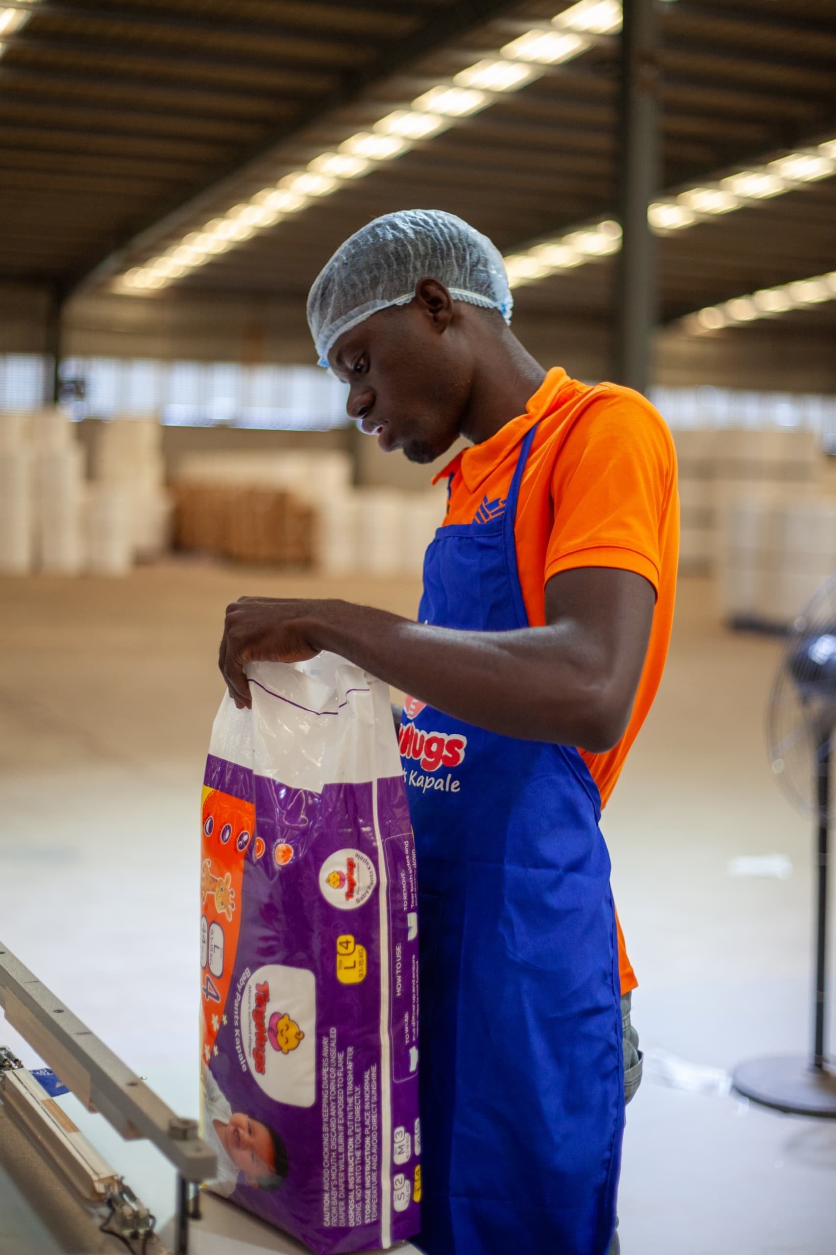 A Pearl Of Africa Hygiene worker in a Tiny Hugs apron checking a finished pack at the plant